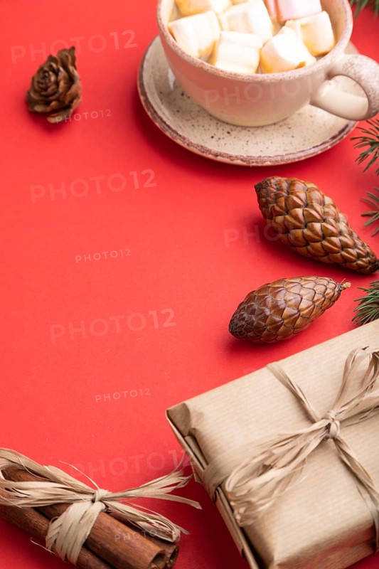 Christmas or New Year composition. Decorations, box, cinnamon, cones, fir and spruce branches, cup of coffee, on a red paper background. Side view, copy space