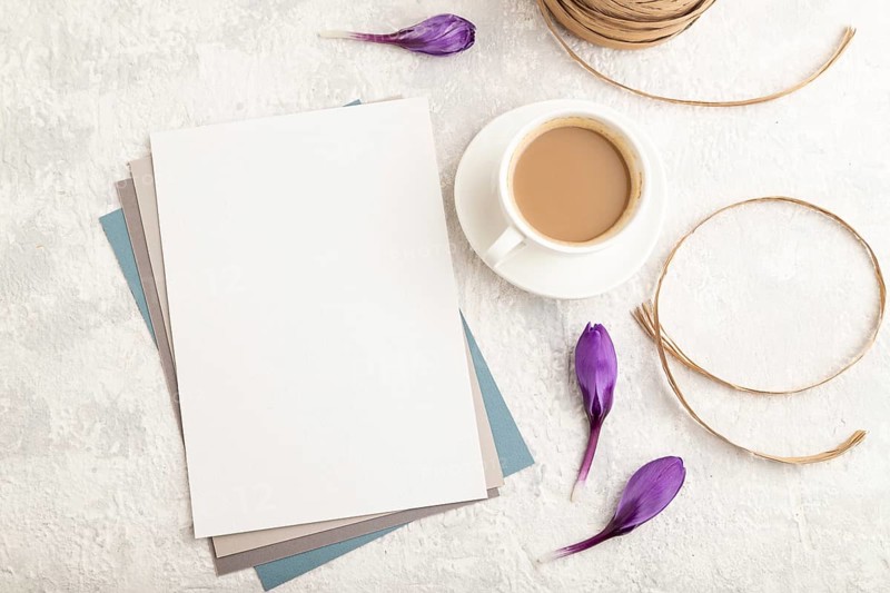 White paper sheet mockup with spring snowdrop crocus flowers and cup of coffee on gray concrete background. Blank, business card, top view, flat lay, copy space, still life. spring concept