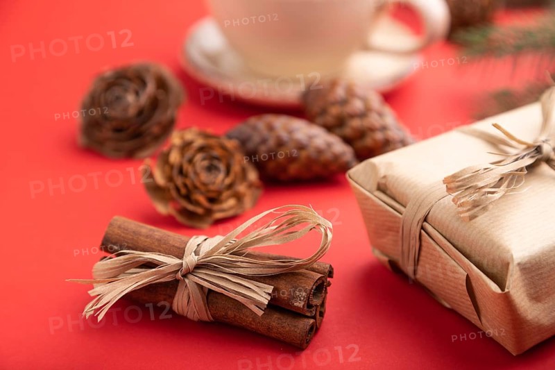 Christmas or New Year composition. Decorations, box, cinnamon, cones, fir and spruce branches, cup of coffee, on a red paper background. Side view, close up, selective focus