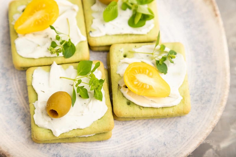 Green cracker sandwiches with cream cheese and cherry tomatoes on gray concrete background. top view, flat lay, close up