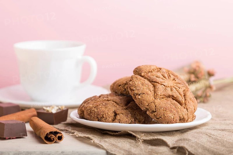 Homemade oatmeal cookies with a cup of cocoa on a linen textile and pink pastel background. side view, close up, selective focus