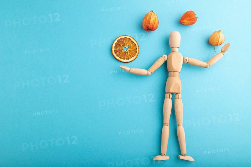 Wooden mannequin juggling dried citrus and physalis on blue pastel background. copy space, isolated