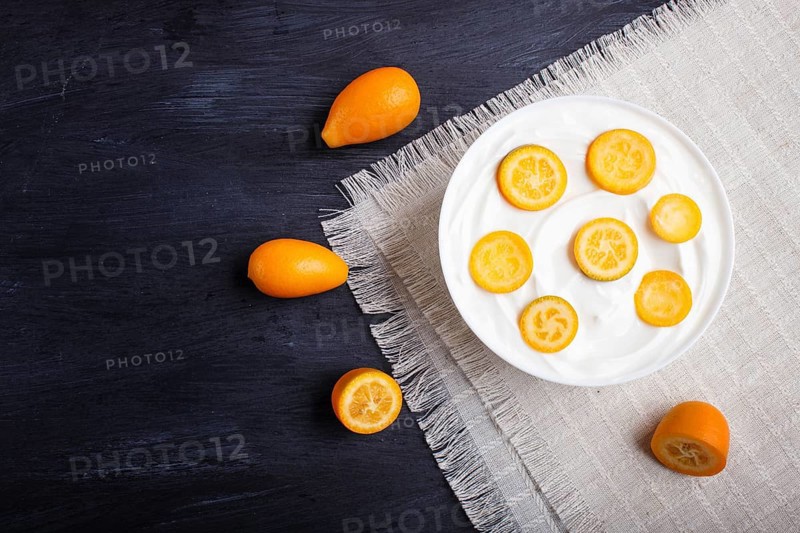 Greek yogurt with kumquat pieces in a white plate on a black wooden background, top view, flat lay, copy space