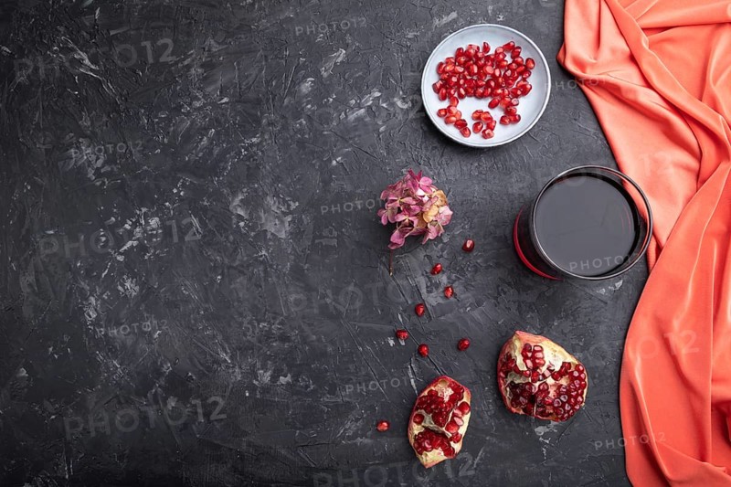 Glass of pomegranate juice on a black concrete background with red textile. Top view, copy space, flat lay