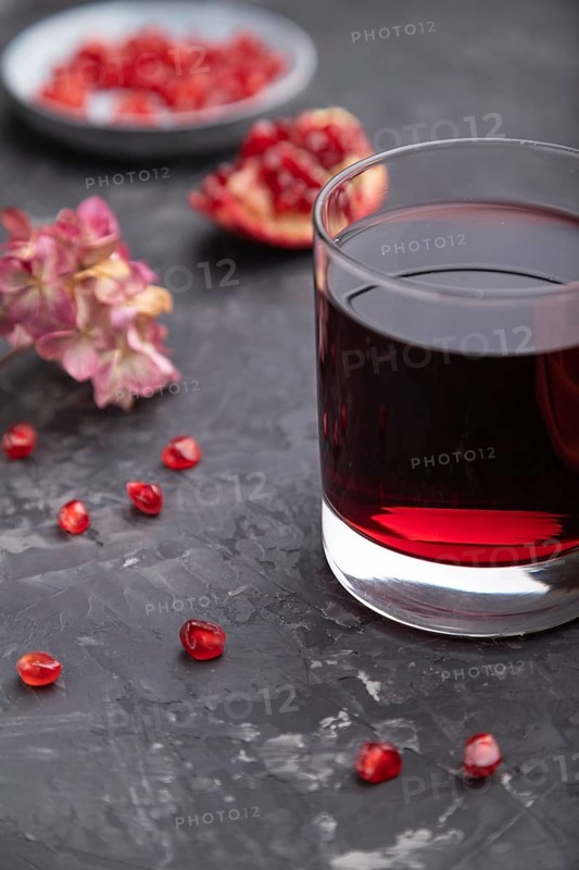 Glass of pomegranate juice on a black concrete background with red textile. Side view, close up, selective focus