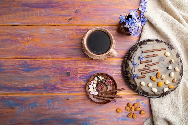 Homemade chocolate brownie cake with caramel cream and almonds with cup of coffee on a colored wooden background and linen textile. top view. flat lay, copy space