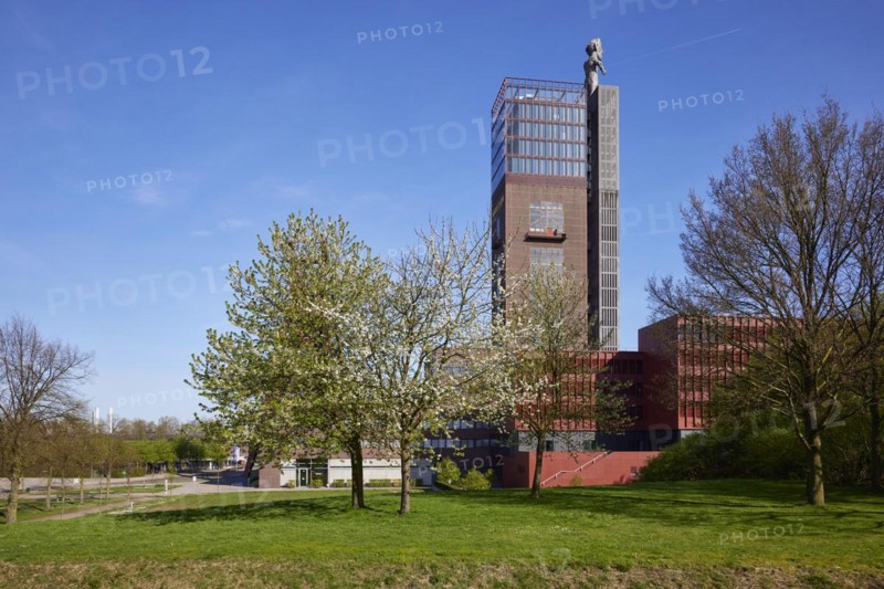 Tower of Nordstern colliery with statue of Hercules and delicately blossoming cherry tree (Prunus) as well as trees without leaves in winter in Nordsternpark, Gelsenkirchen, Ruhr area, independent city, North Rhine-Westphalia, Germany, Europe