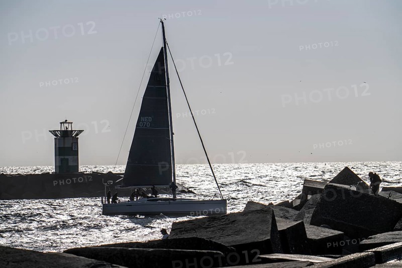Sailing boat leaving the harbour of Scheveningen, lighthouse at the harbour entrance, Netherlands