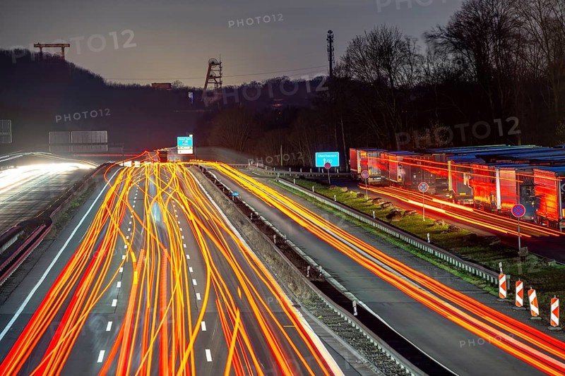 Evening traffic on the A2 motorway at the Recklinghausen junction heading west, in the background the headframes of the former Ewald colliery, Hohenhorst rest area, overflowing with lorries, North Rhine-Westphalia, Germany, Europe