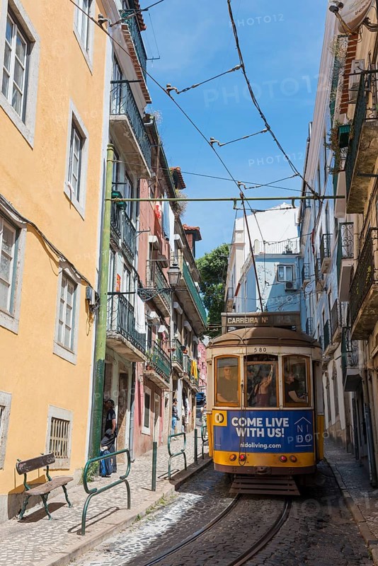 A yellow-blue tram runs through a narrow street past colourful, historic buildings on a sunny day, Tram, Line 28, Carros eléctricos de Lisboa, Eléctricos de Lisboa, Old Town, Lisbon, Portugal, Europe