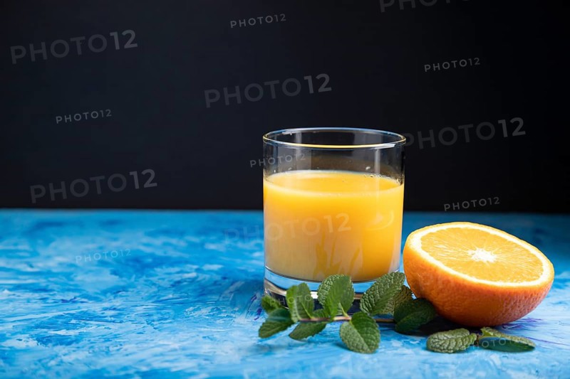 Glass of orange juice with mint on a black and blue background. Hard light, contrast. Side view, copy space