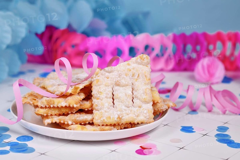 Fried Italian dessert snack for carnival season called 'Galani', ' Chiacchiere' or 'Crostoli' depending on region with paper streamers in background. Also known as Angel Wings pastry