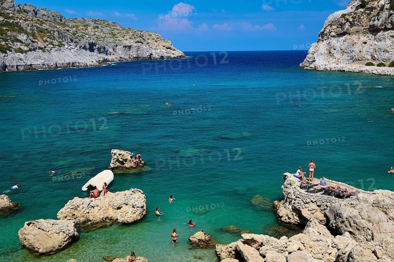 Sunbathing people on rocks on a coast with deep blue water and sunny sky, Anthony Quinn Bay, Vagies Bay, Rhodes, Dodecanese, Greek Islands, Greece, Europe