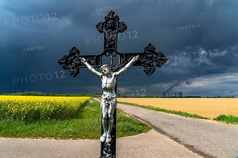 Cross commemorates the former monastery church of St. Luzia, Bedburg-Frauweiler, from 1488, it was blown up in 1970 to make way for the former Fortuna-Garsdorf open-cast lignite mine, Neurath lignite-fired power plant, near Grevenbroich, RWE Power AG, storm clouds over the Rhenish lignite mining area, rape field, North Rhine-Westphalia, Germany, Europe
