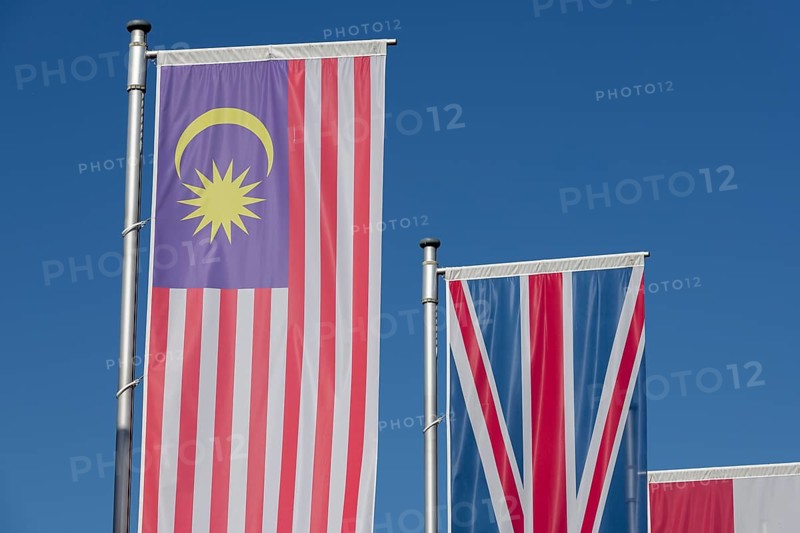 Several flags of different countries fly side by side under a clear blue sky, Malaysian flag, English flag