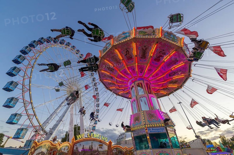 A funfair at dusk with illuminated chain carousel and Ferris wheel, Europa Rad, rides, wave flight, Cannstatter Wasen, folk festival, Bad Cannstatt, Stuttgart, Baden-Württemberg, Germany, Europe