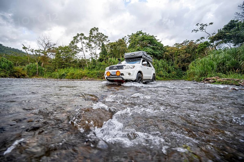 Toyota off-road vehicle with roof tent drives through a wide river in the rainforest, Alajuela province, Costa Rica, Central America