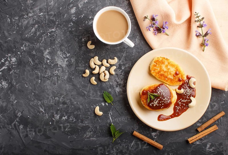 Cheese pancakes with caramel sauce on a beige ceramic plate and a cup of coffee on a black concrete background. top view, flat lay, copy space