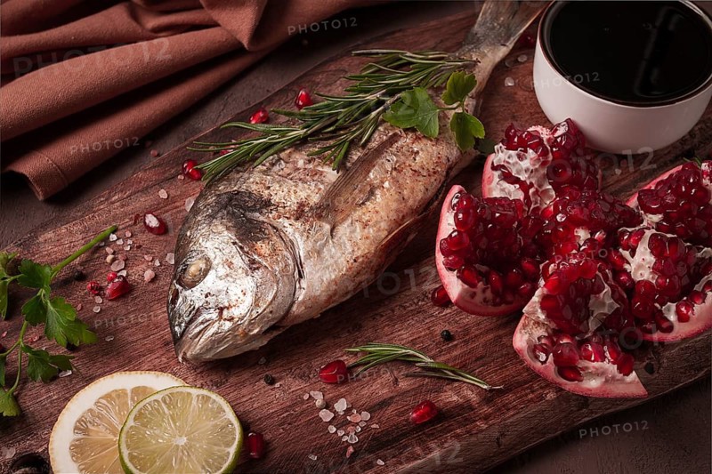 Fried dorado fish, with spices and herbs, on a wooden board, pomegranate sauce, close-up, no people