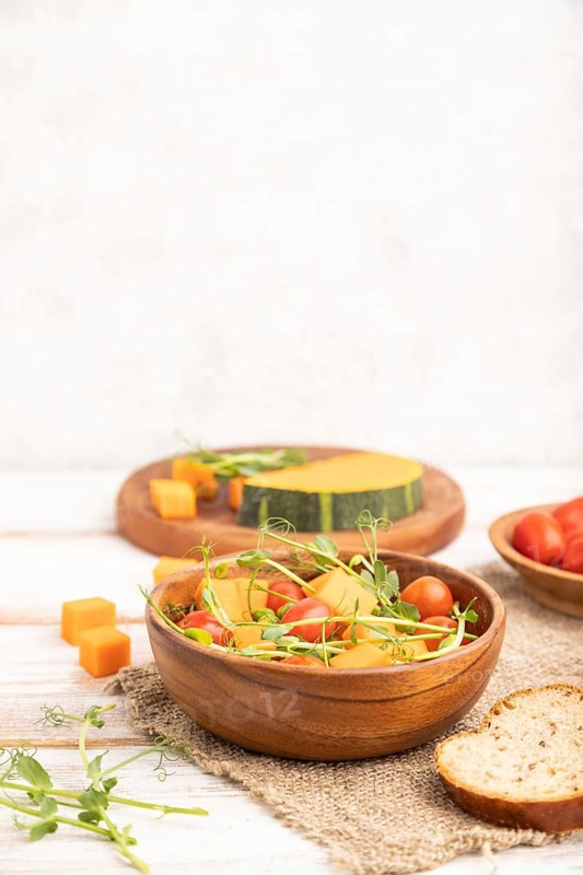 Vegetarian vegetable salad of tomatoes, pumpkin, microgreen pea sprouts on white wooden background and linen textile. Side view, copy space