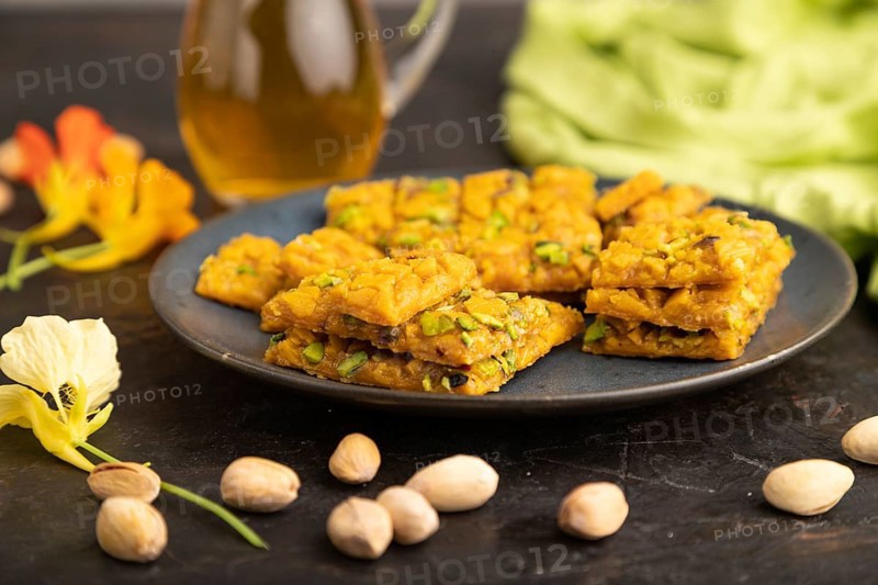 Traditional iranian dessert sohan with glass of green tea on a black concrete background and green textile. side view, close up, selective focus