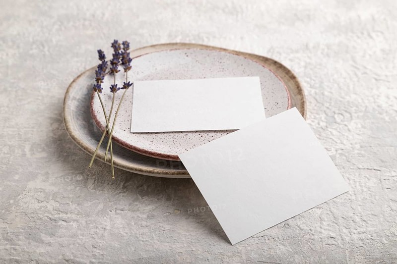 White paper invitation card, mockup with lavender on ceramic plate and gray concrete background. Blank, side view, still life, copy space