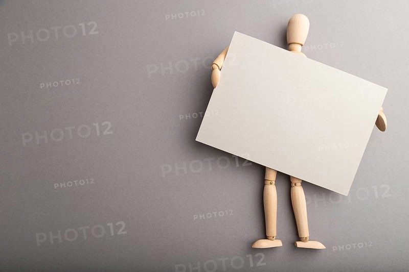 Wooden mannequin holding gray blank poster on gray pastel background. copy space, isolated, presentation concept