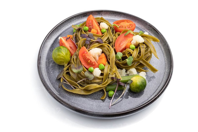 Tagliatelle green spinach pasta with tomato, pea and microgreen sprouts isolated on white background. Side view, close up