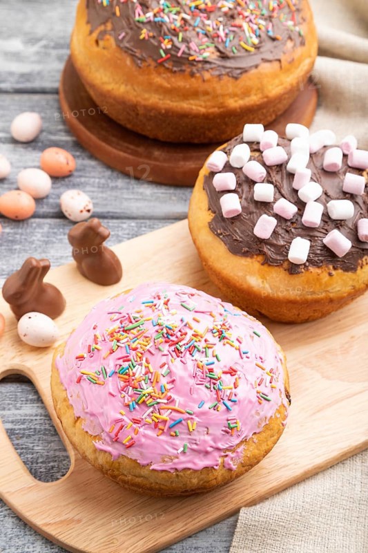 Homemade glazed and decorated easter pies with chocolate eggs and rabbits on a gray wooden background and linen textile. Side view, copy space