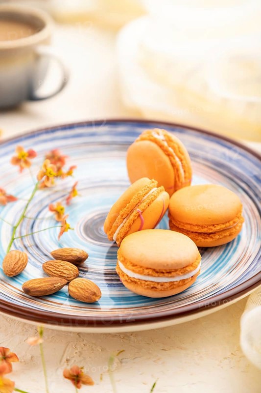 Orange macarons or macaroons cakes with cup of coffee on a white concrete background and linen textile. Side view, close up, selective focus