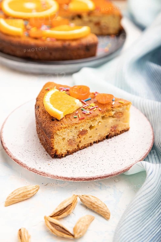 Orange cake with almonds and a cup of coffee on a white concrete background and blue linen textile. Top view, close up, selective focus