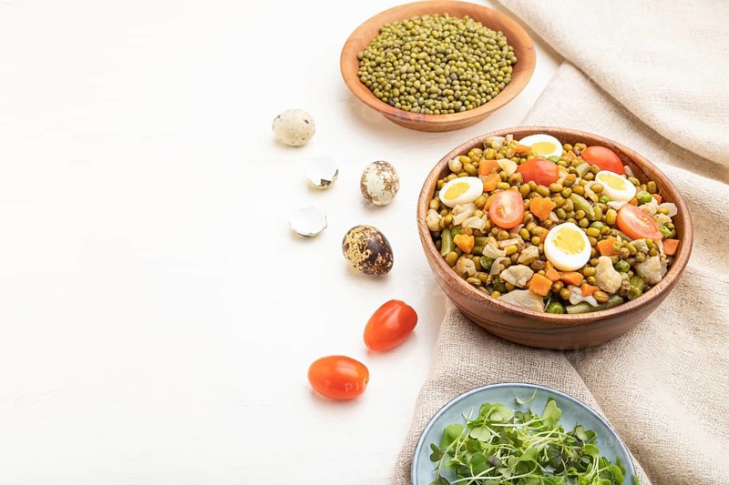 Mung bean porridge with quail eggs, tomatoes and microgreen sprouts on a white wooden background and linen textile. Side view, copy space