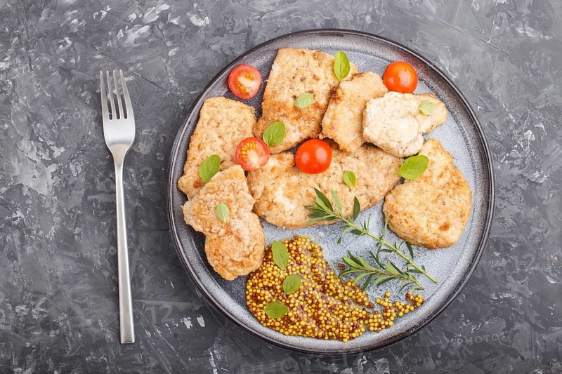 Fried pork chops with tomatoes and herbs on a gray ceramic plate on a black concrete background. top view, flat lay, close up