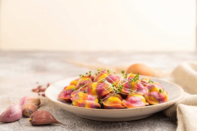 Rainbow colored dumplings with pepper, herbs, microgreen on brown concrete background and linen textile. Side view, selective focus, copy space