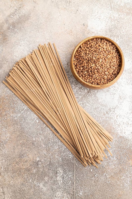 Japanese buckwheat soba noodles with tomato, eggs, spices, herbs on brown concrete background. Top view, flat lay, close up
