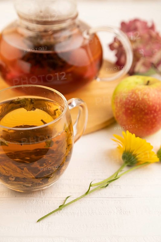 Red tea with herbs in glass teapot on white wooden background. Healthy drink concept. Top view, close up, selective focus