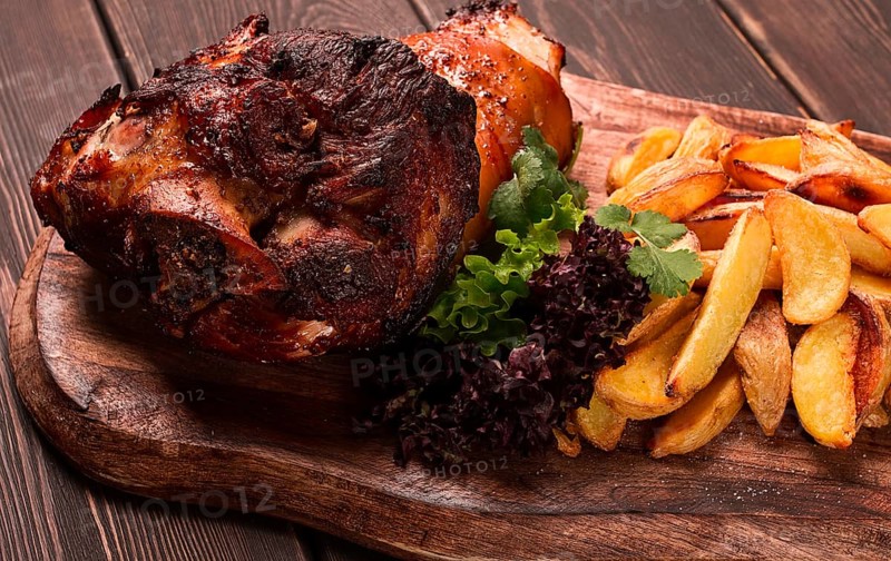 Pork knuckle, in soy-honey sauce, with fried potatoes, on a wooden chopping board, homemade, no people