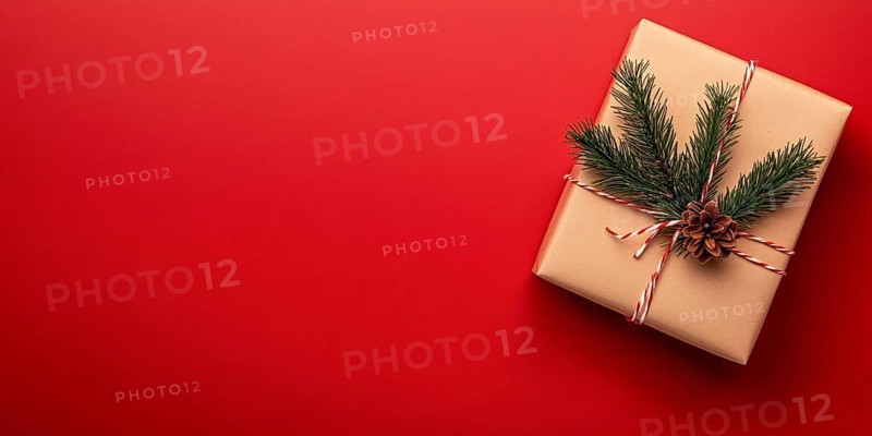 Banner with small Christmas gift box wrapped in kraft paper with fir branch on side of red background with copy space. Generative Ai, AI generated