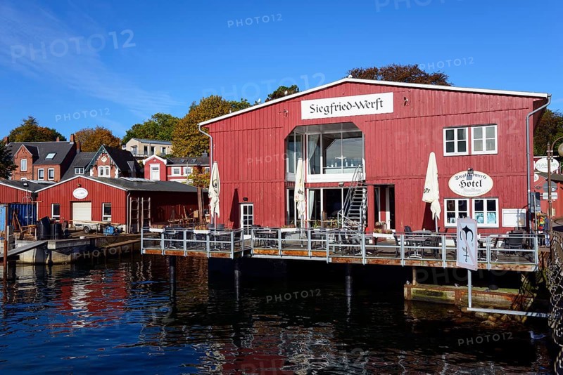 A red wooden building with 'Hotel' lettering on the waterfront under a clear blue sky on a sunny day, Siegfried-Werft, Eckernförde, Schleswig-Holstein, Germany, Europe