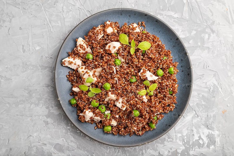 Quinoa porridge with green pea and chicken on ceramic plate on a gray concrete background. Top view, flat lay, close up
