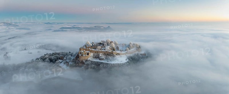 Aerial panorama of the Hegau volcano Hohentwiel with Germany's largest fortress ruins on a cold, foggy winter morning, in front of sunrise, on the horizon seen from the left the Hegau mountains Hohenstoffeln, Hohenhewen, Mägdeberg and Hohenkrähen, Singen am Hohentwiel, district of Constance, Baden-Württemberg, Germany, Europe