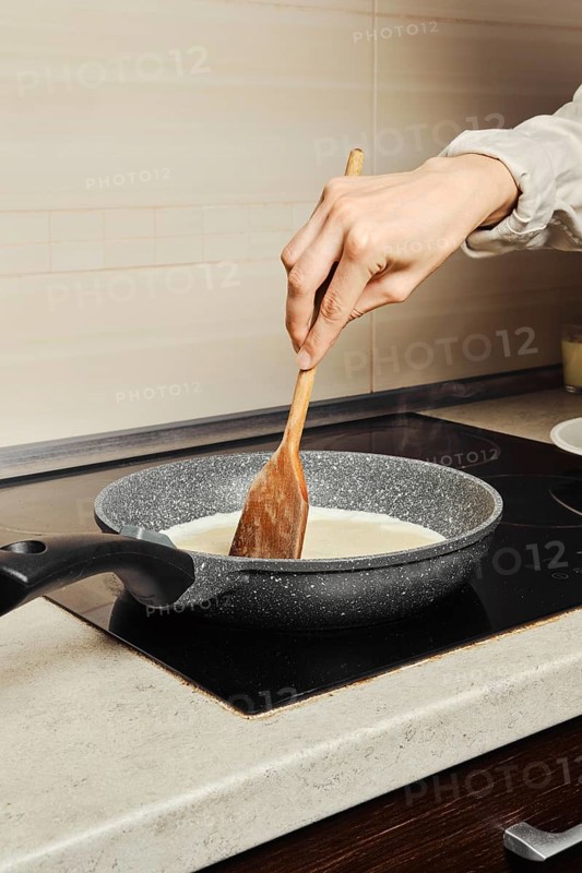 Unrecognizable woman miking scrambled eggs in a frying pan in her kitchen