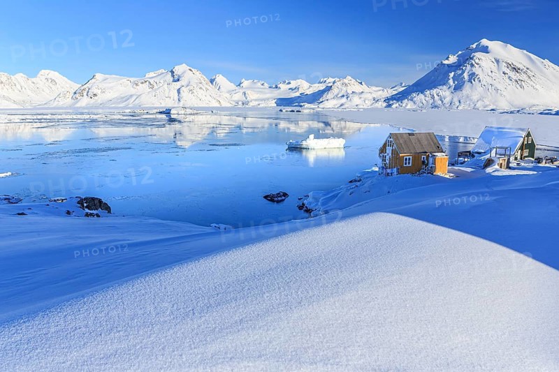 Inuit settlement, houses in front of icebergs in icy fjord, mountains, winter, snow, sunny, Kulusuk, East Greenland, Greenland, North America