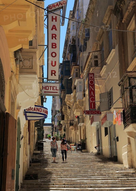 Steps climb hill of narrow street historic housing with traditional balconies in city centre of Valletta, Malta, Europe