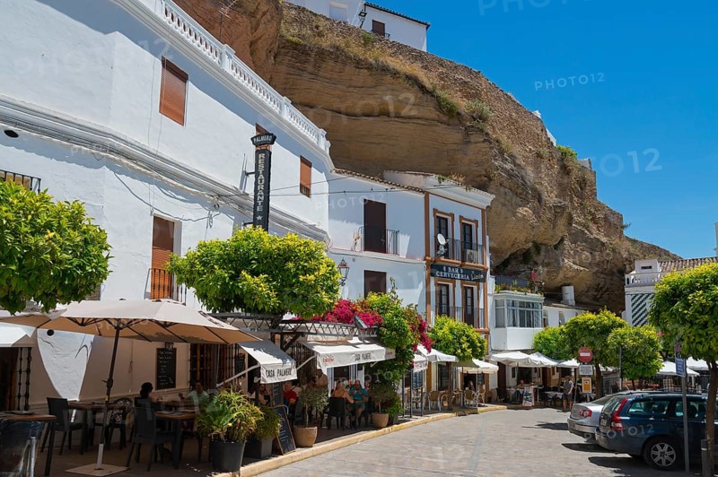 Street with cars and restaurants under rocks with white houses, sunny sky in Setenil de las Bodegas, cave flats, Setenil de las Bodegas, Cadiz, Andalusia, Spain, Europe