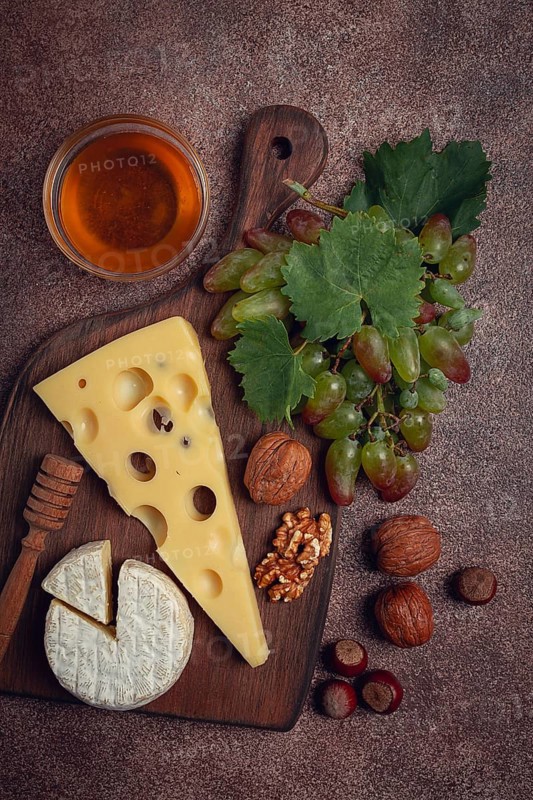 Cheese with big holes, emmental, maasdam, brie cheese, on a cutting board, with grapes and honey, nuts, appetizer to wine, top view