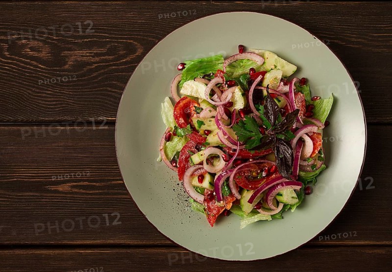 Georgian vegetable salad, tomatoes with cucumbers, red onion, walnut, pomegranate seeds, top view, no people
