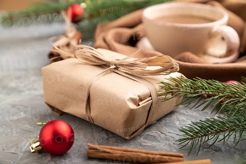Christmas or New Year composition. Decorations, box, cinnamon, fir and spruce branches, cup of coffee, wool scarf on a gray concrete background. Side view, close up, selective focus