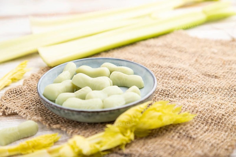 Jelly celery candies on white wooden background and linen textile. close up, side view, selective focus