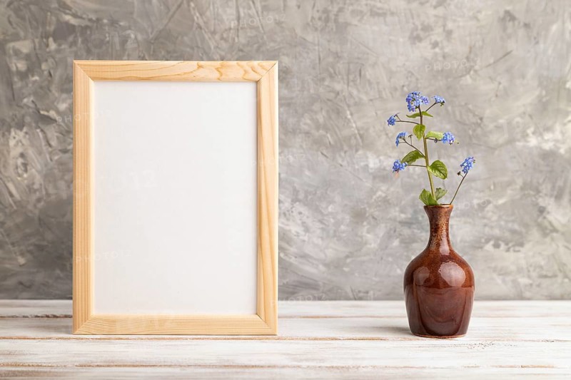 Wooden frame with blue forget-me-not flowers in ceramic vase on gray concrete background. side view, copy space, still life, mockup, template, spring, summer minimalism concept